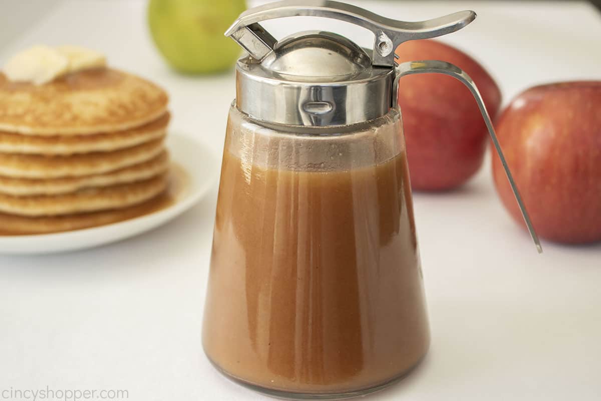 Pour jar with apple syrup, pancakes and apples.