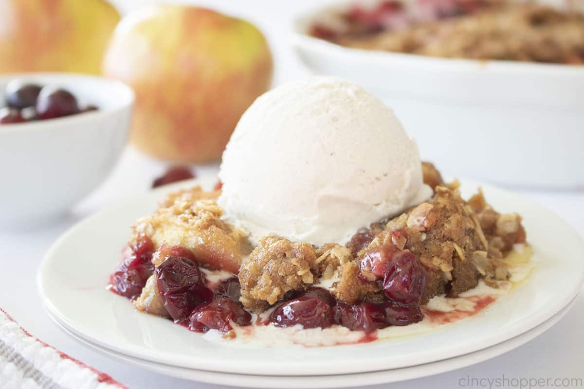 Plate of apple crisp with cranberries and topped with ice cream.