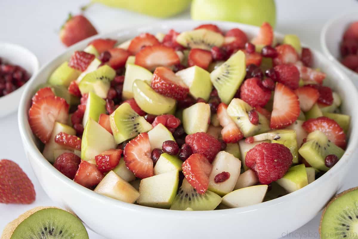 Red and green winter fruit salad in a white bowl.
