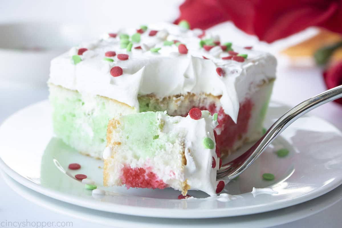 Poke cake for Christmas with red and green Jello on a plate with a fork.
