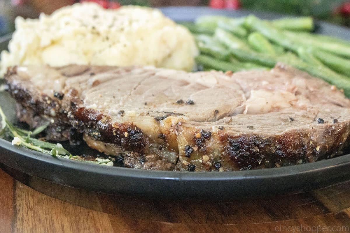 Prime Rib with crust on a plate with mashed potatoes and green beans.