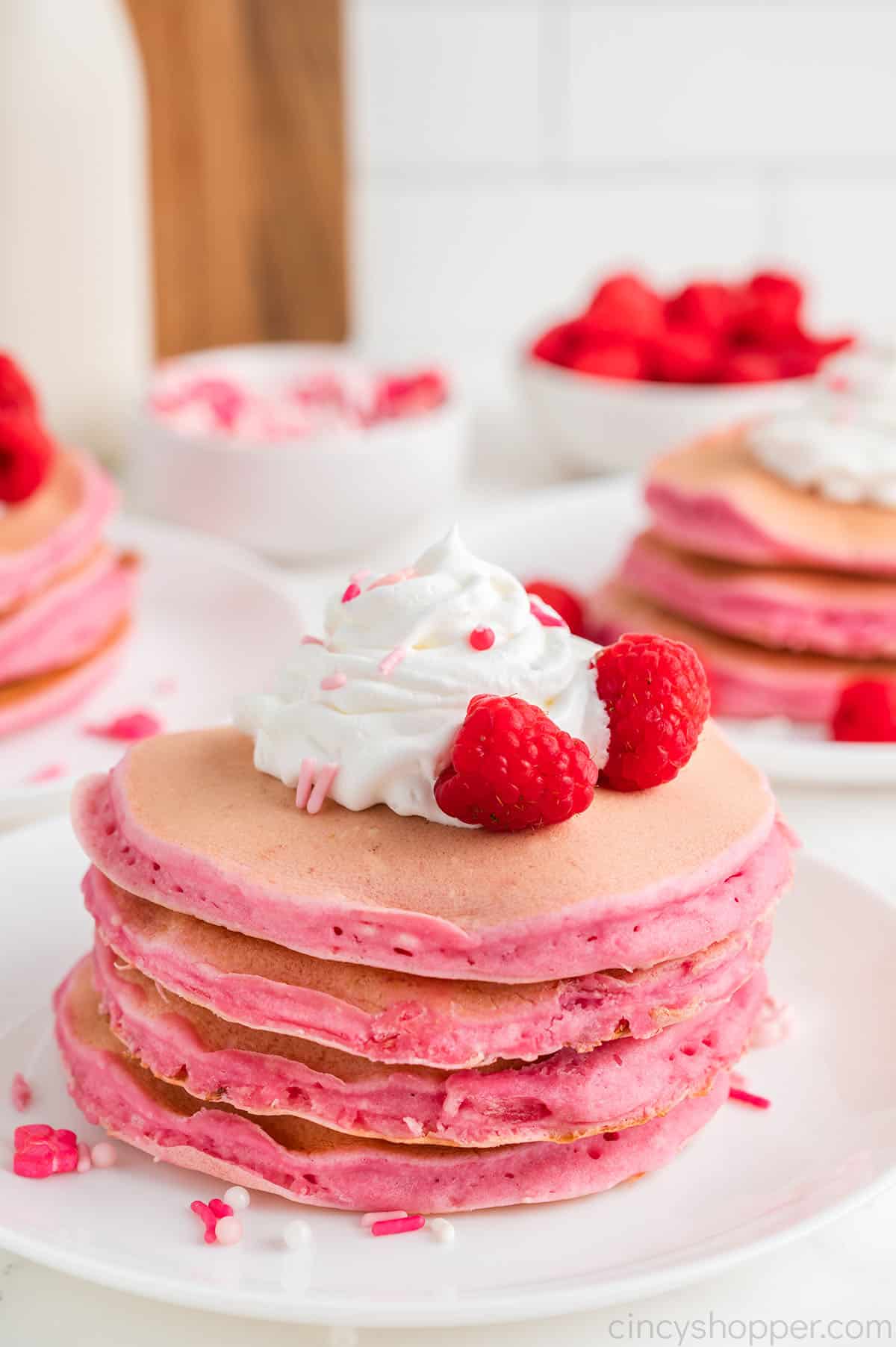 Stack of Pink Valentine Pancakes with whipped topping, sprinkles and raspberries.