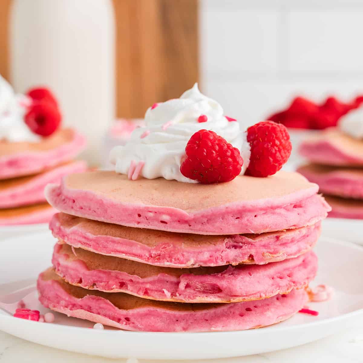 Pink Pancakes with whipped topping and fruit on a white plate.