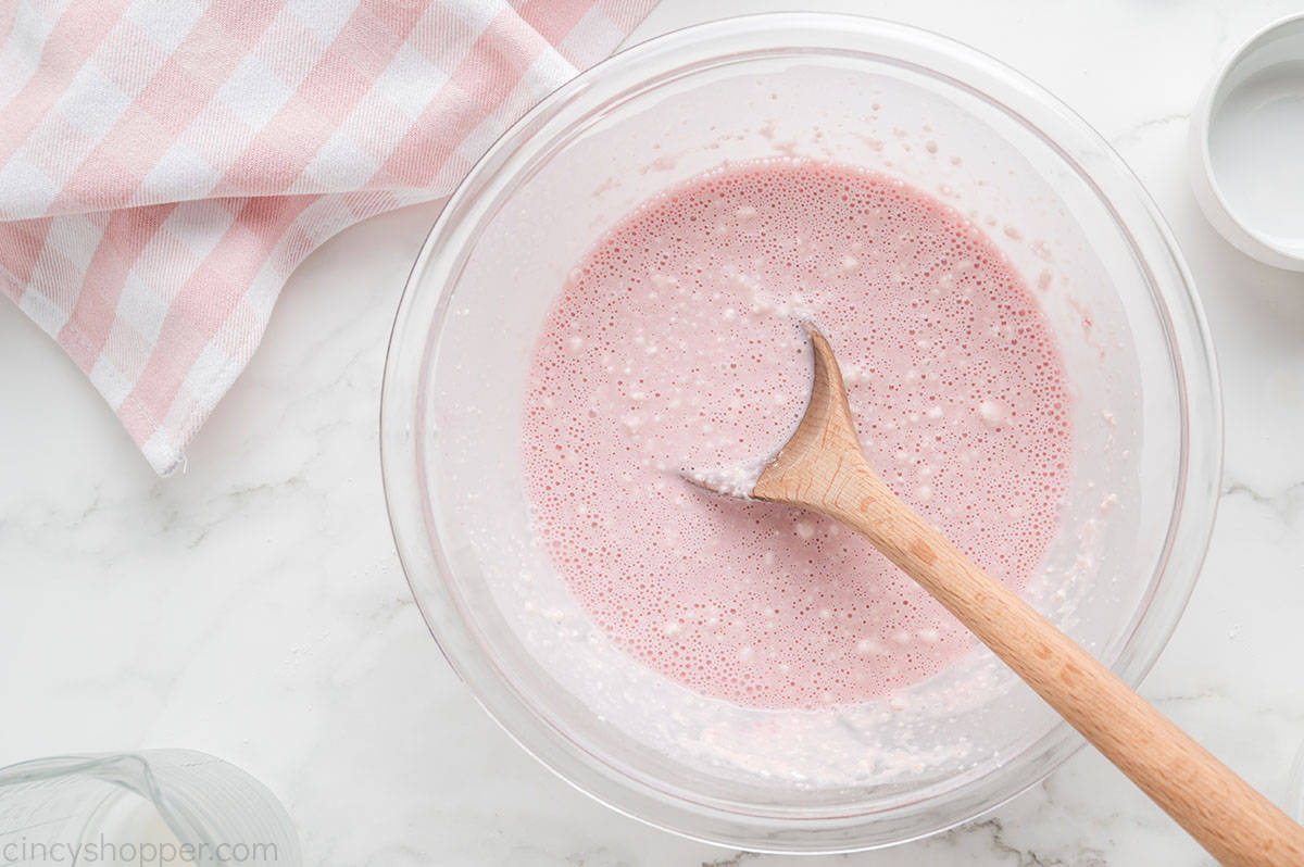 Pink pancake batter in a clear bowl with wooden spoon.