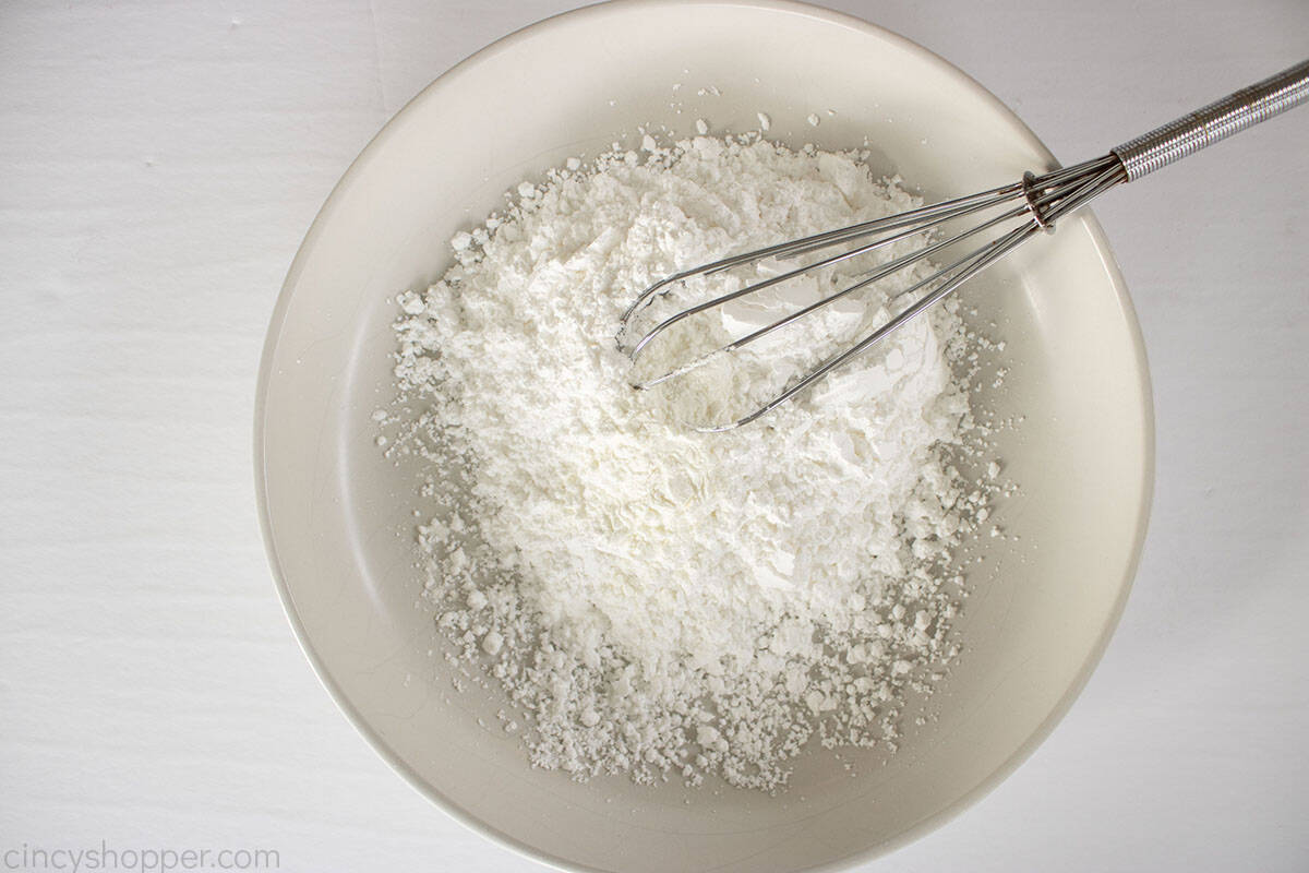 Powdered sugar and cornstarch in a white bowl with whisk.