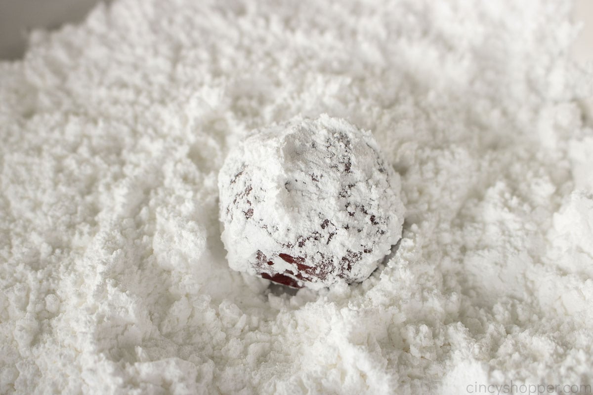 Red velvet cookie dough ball in powdered sugar mixture.
