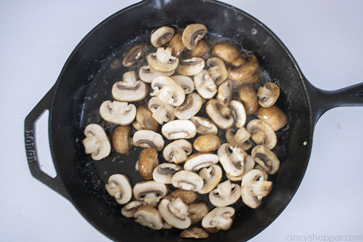 Mushrooms frying in a cast iron skillet.
