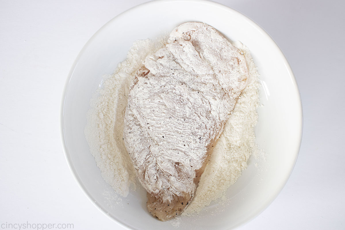 Chicken breast in a white bowl with flour.
