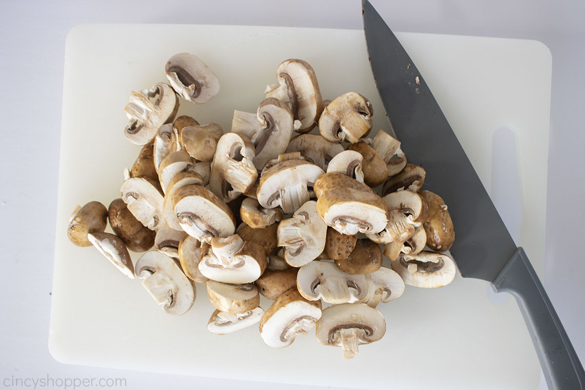 Sliced mushrooms on a white cutting board with a gray knife.