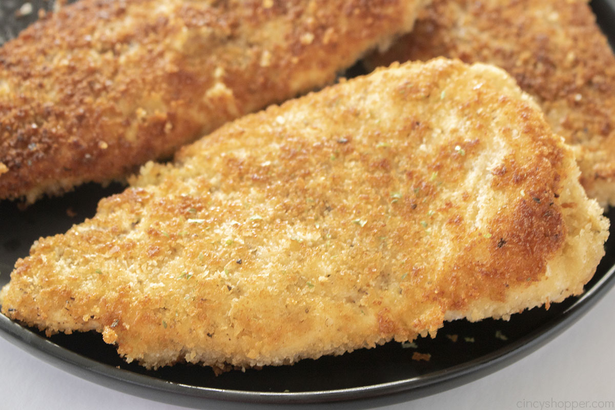 Panko chicken breast whole on a black plate.