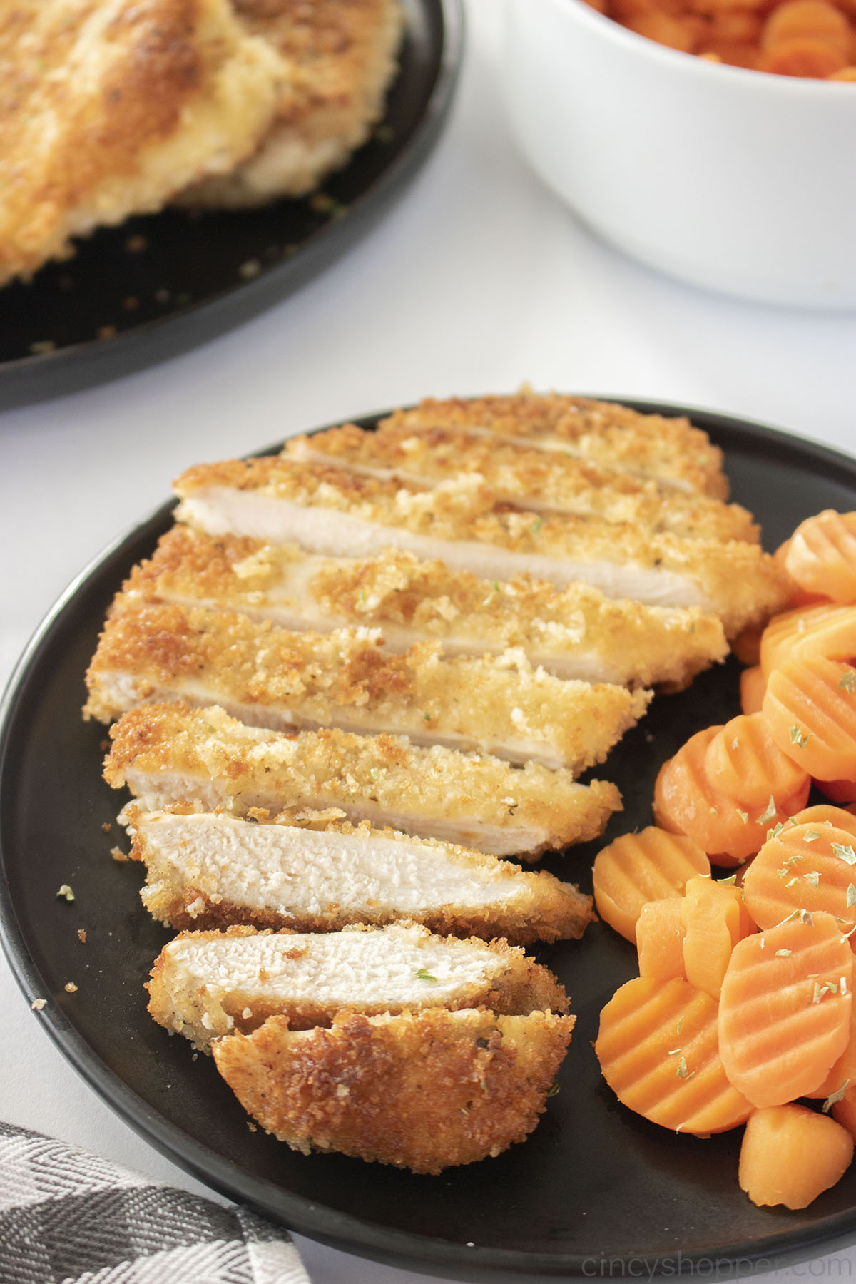 Panko chicken cut in slices on a black plate with carrots.