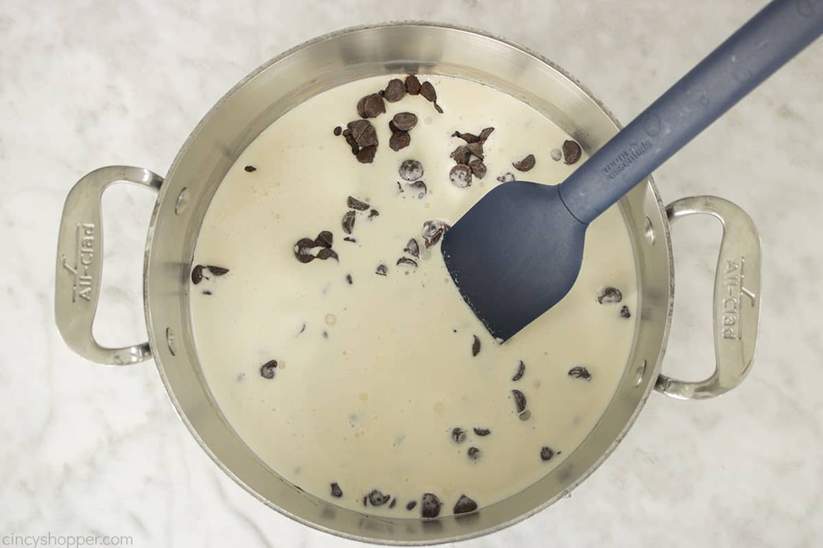 Chocolate chips, heavy cream and salt in a sauce pan with a blue spatula.