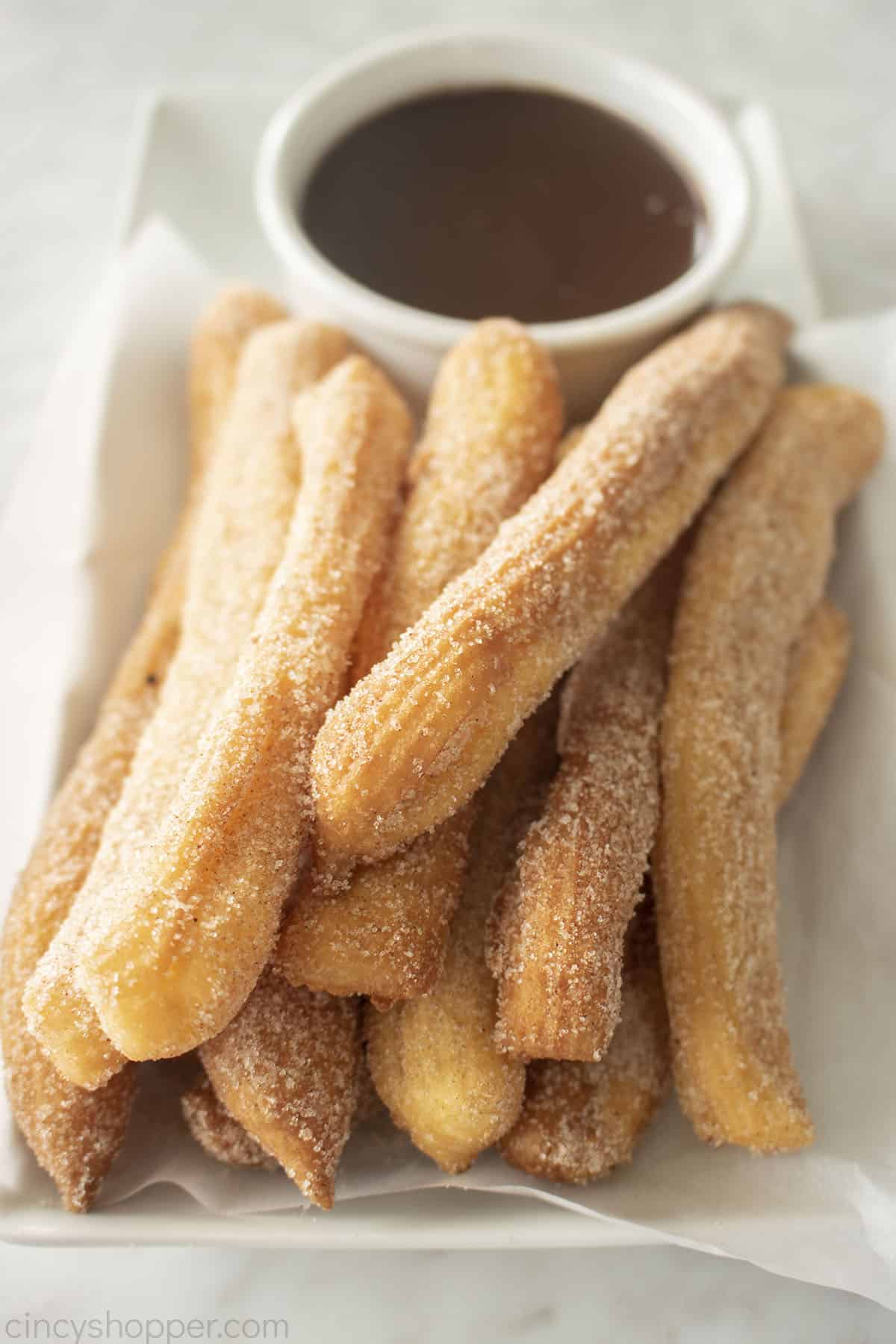 Fried authentic Mexican Churros on a white platter with chocolate dipping sauce.