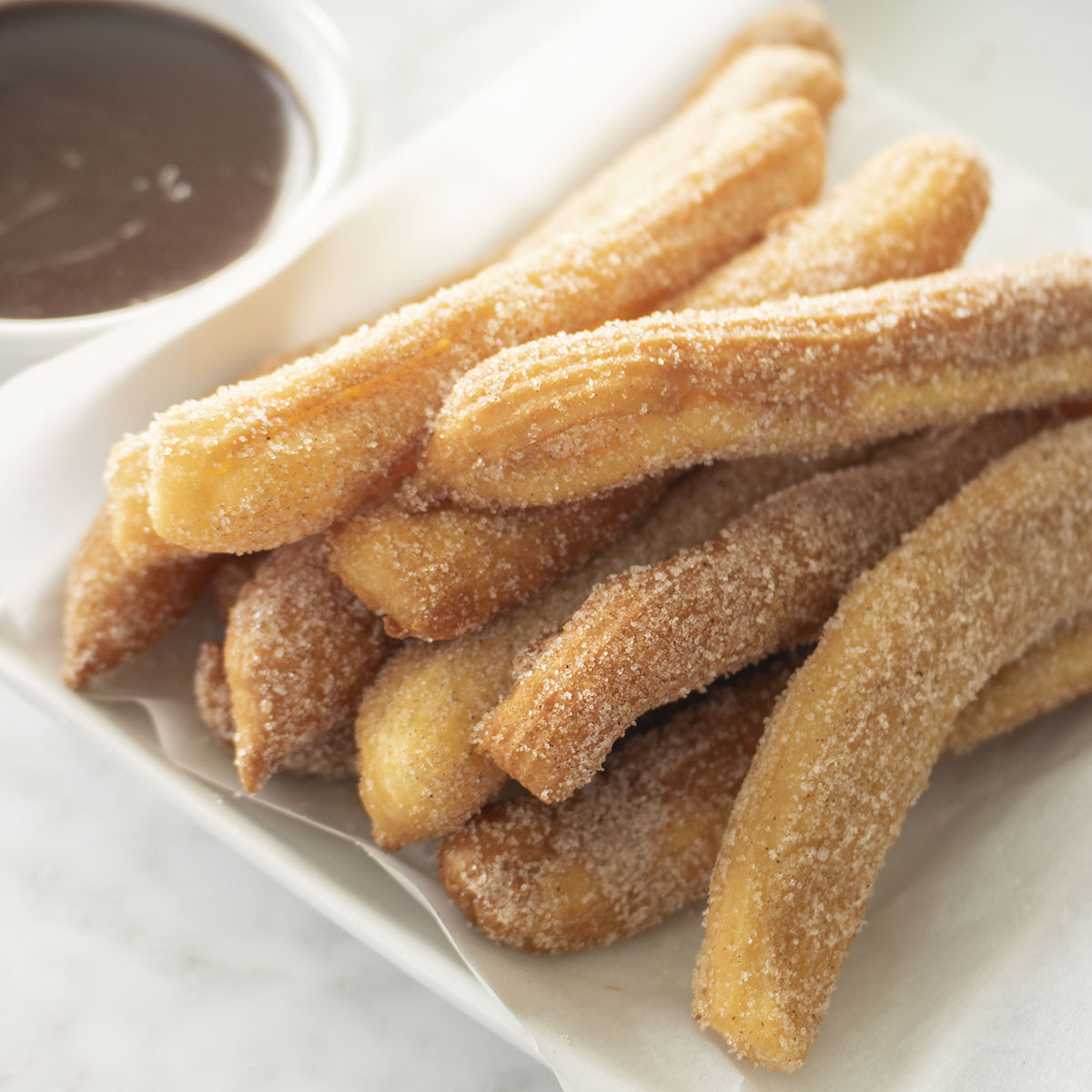 Homemade Mexican Churros on a white platter with chocolate dipping sauce.