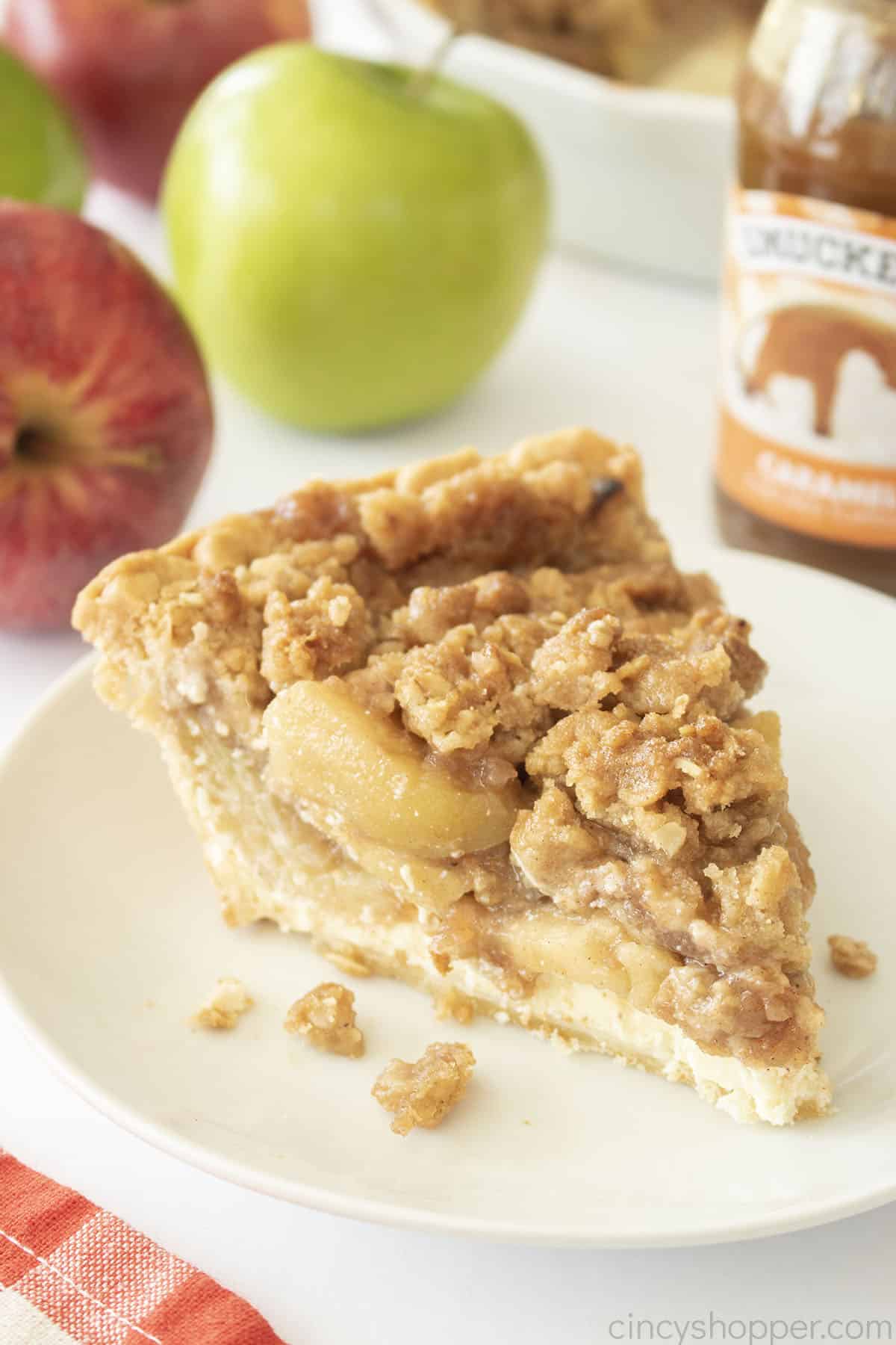 Slice of Apple Pie stuffed Cheesecake on a white plate.