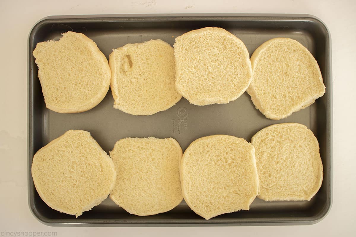 Opened Sesame seed buns on a baking sheet.