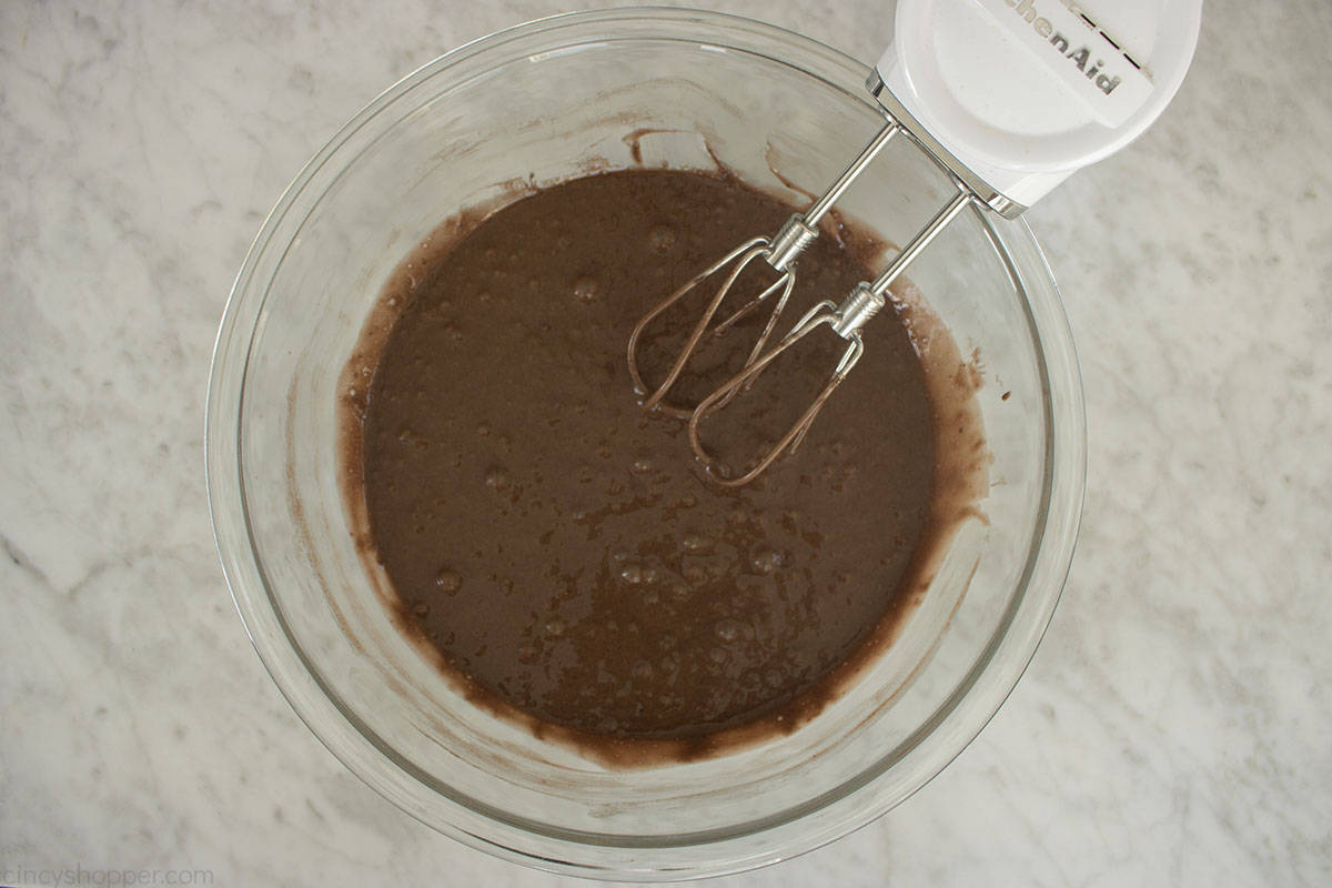 Chocolate cake mix batter in a bowl with a hand mixer.