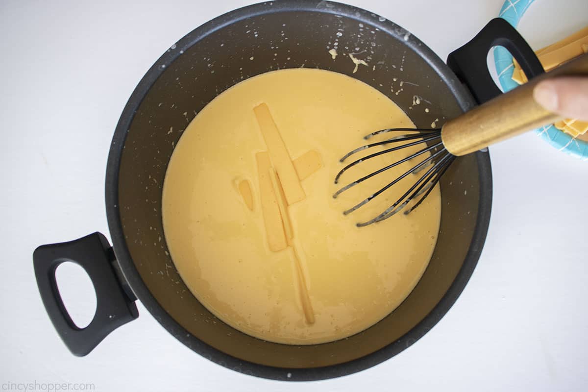 Adding sliced American cheese to mixture with a whisk.