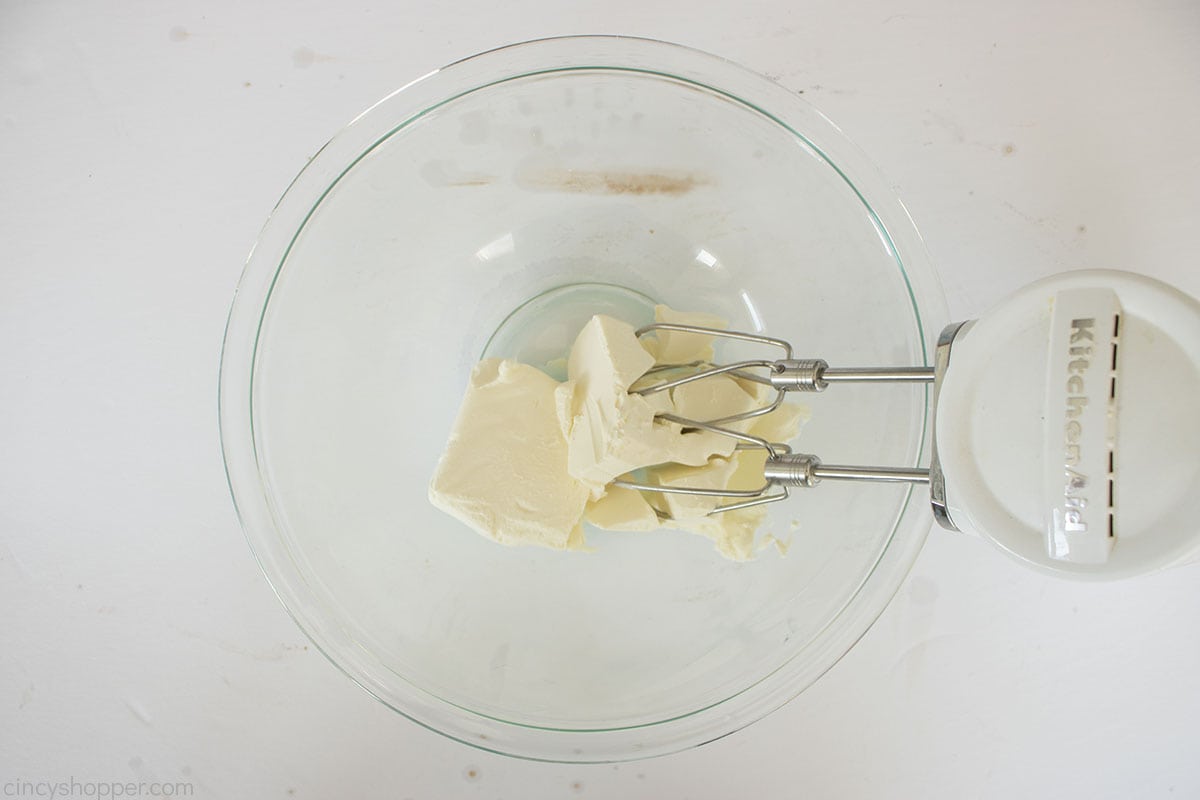 Softened cream cheese in a bowl with a hand mixer.