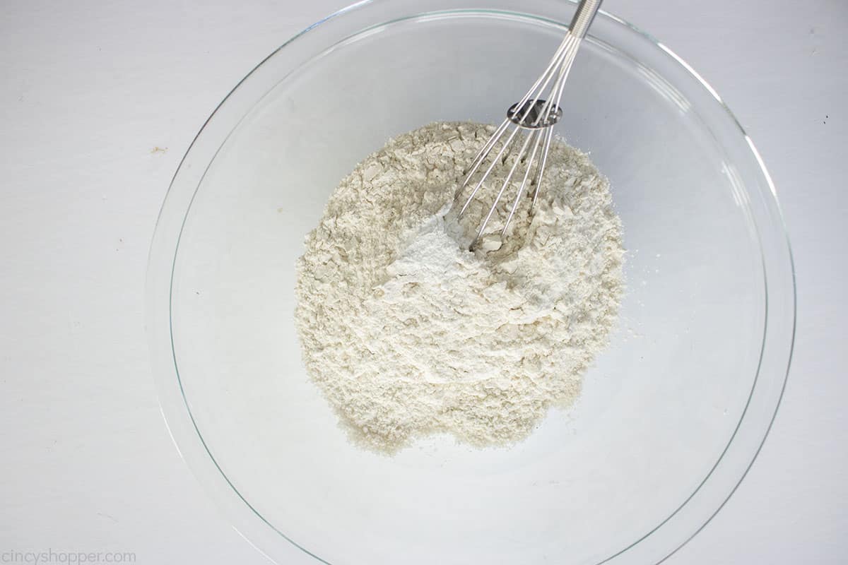 Flour and baking soda in a clear bowl with a whisk.