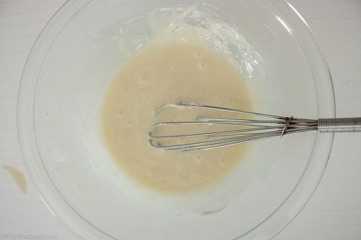 Quick cinnamon roll icing in a clear bowl with a whisk.