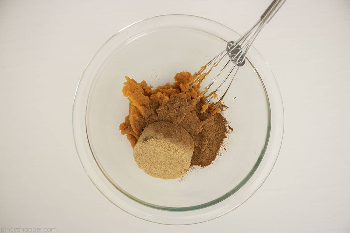 Pumpkin cinnamon roll filling in a clear bowl with a whisk.