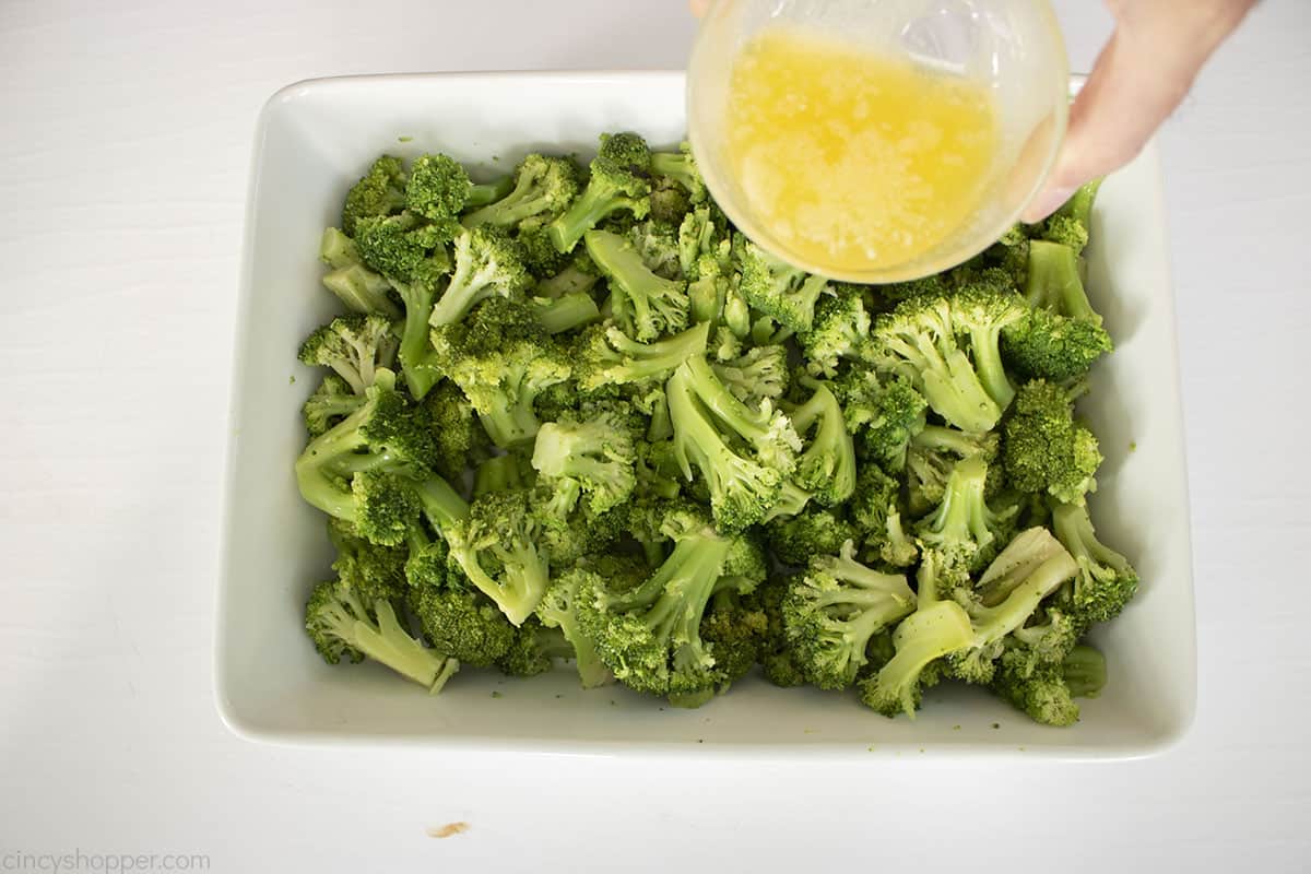 Adding butter to cooked broccoli in a casserole dish.