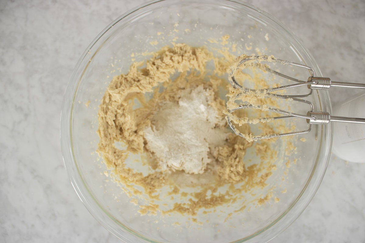 Slowly adding dry ingredients to wet ingredients with a hand mixer.