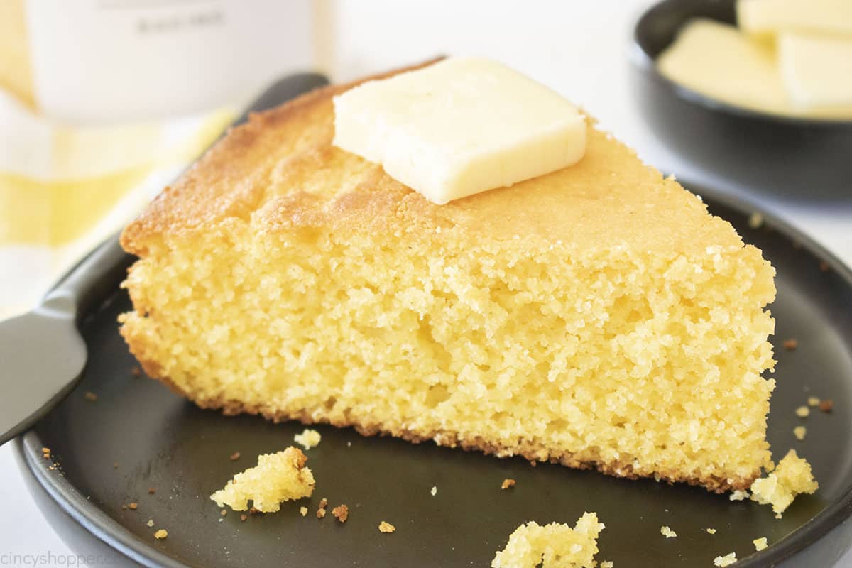 Individual slice of Old Fashioned Corn bread on a black plate with butter and knife.