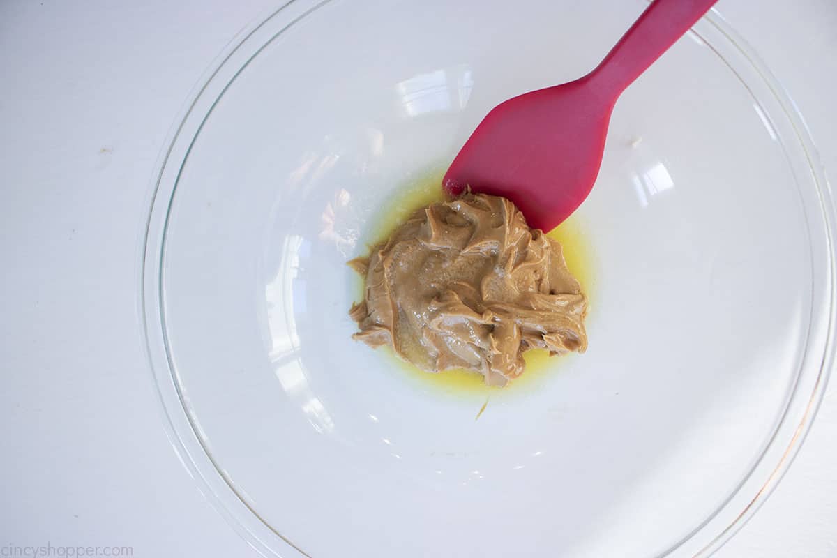 Peanut butter and melted butter in a glass bowl with red spatula.