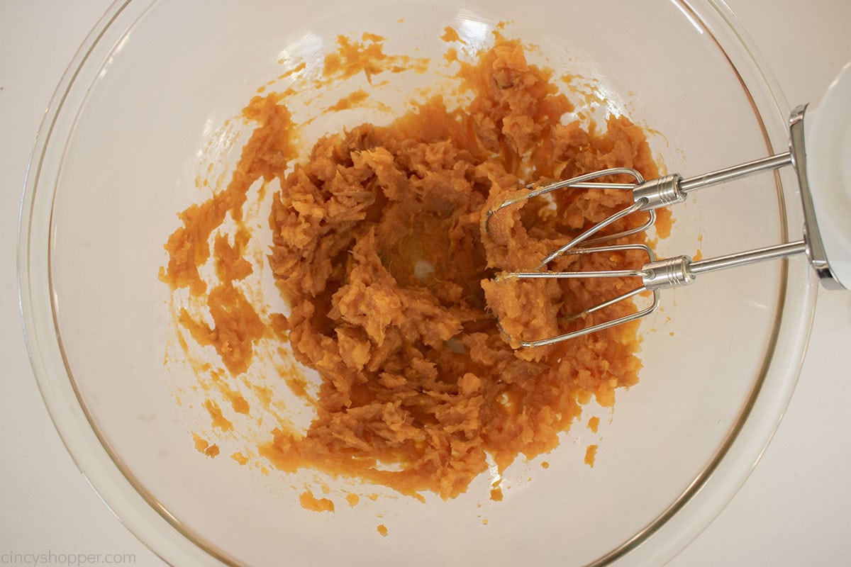 Baked sweet potatoes in a mixing bowl with hand held mixer.