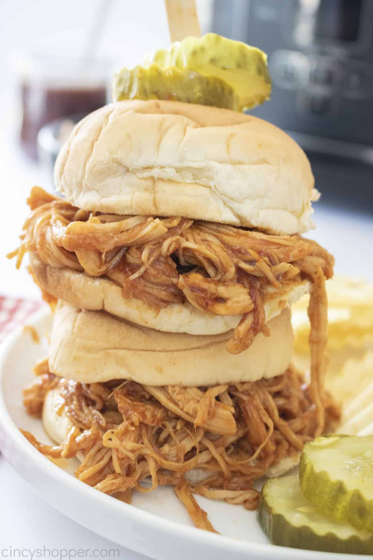 Stack of Slow Cooker BBQ Pulled Chicken Sandwiches on a plate with chips and pickles.