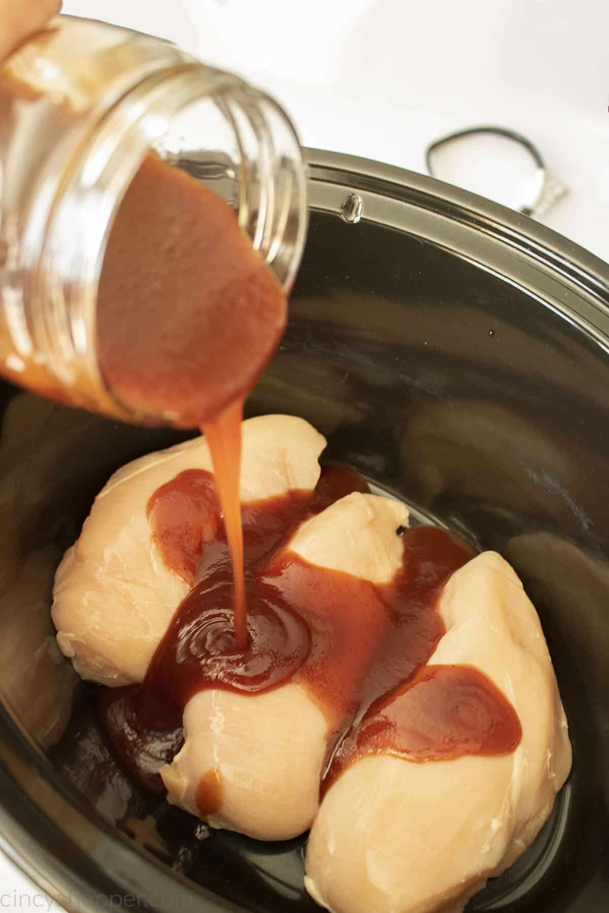 Pouring BBQ sauce on raw chicken in a CrockPot.