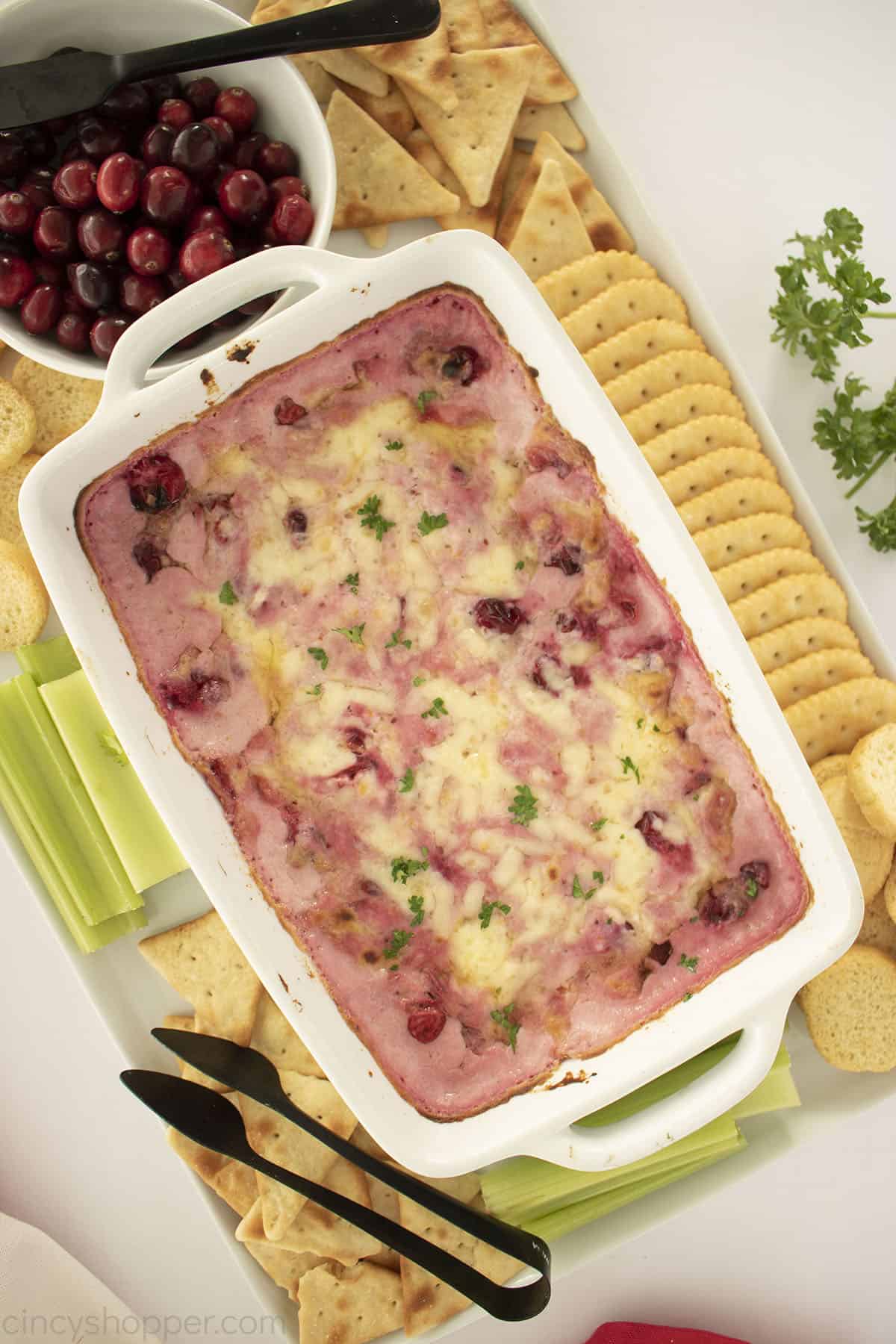 Baked Cranberry Cream Cheese Dip in a white casserole dish with crackers, bread and vegetables. 