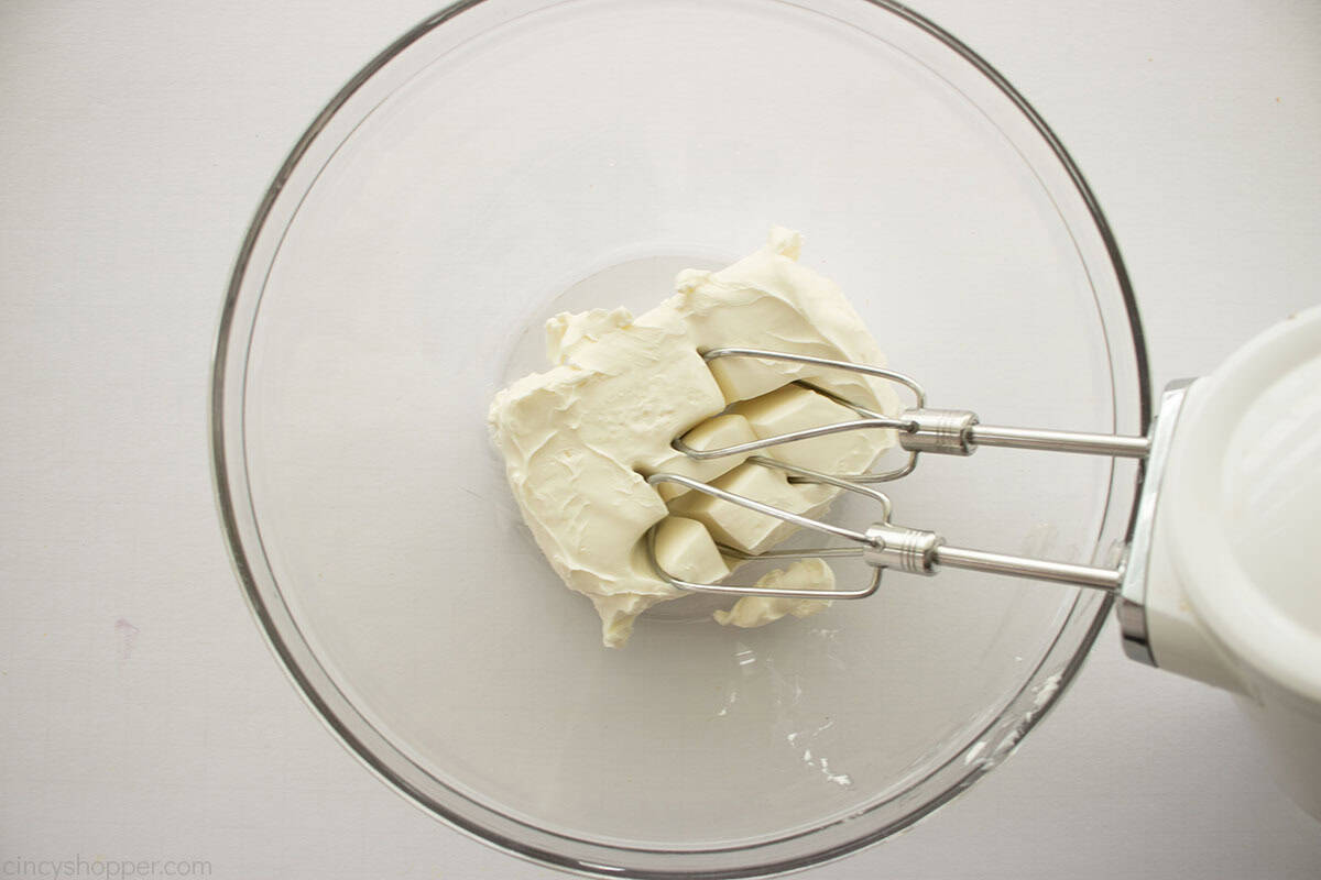 Softened cream cheese in a clear mixing bowl with a hand mixer.