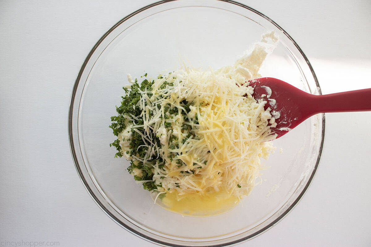 All lasagna cheese mixture in a clear mixing bowl with a red spatula.