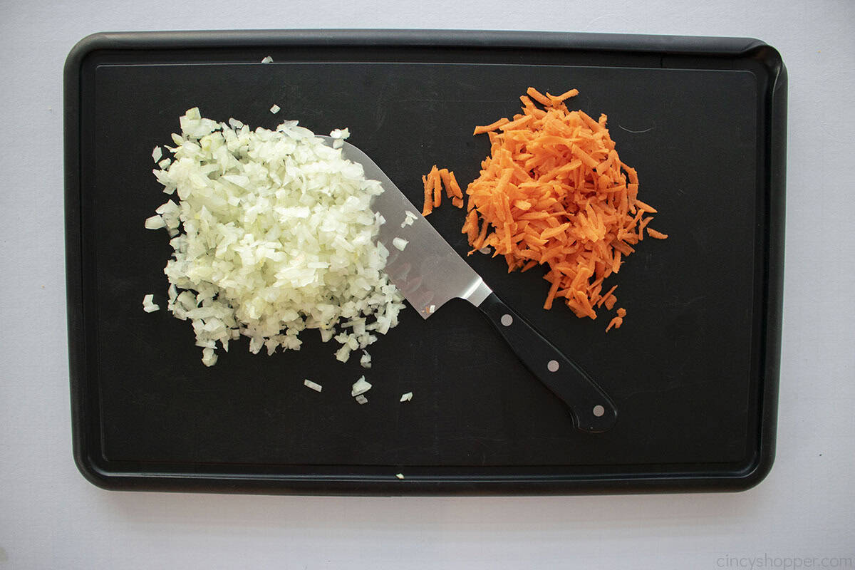 Finely diced onions and carrots on a black cutting board with a knife.