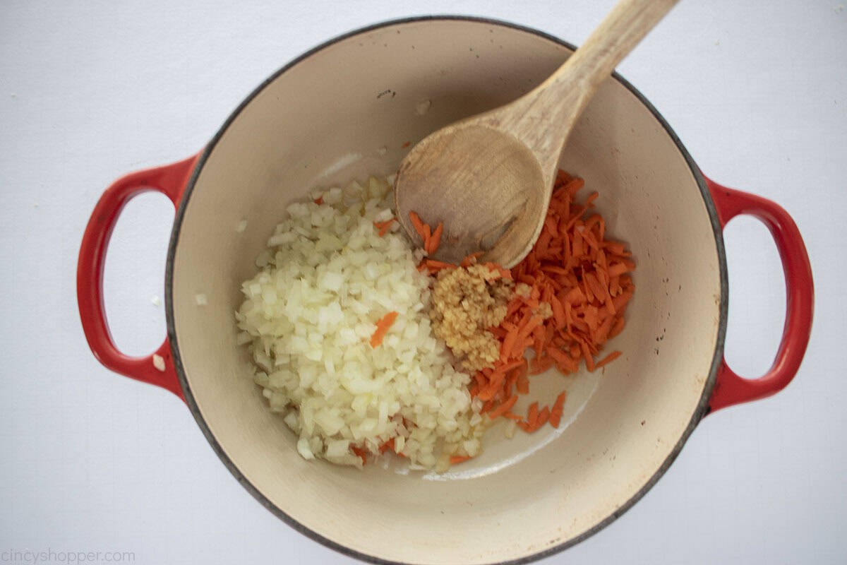 Oil, carrots, onions and garlic in a dutch oven with a wooden spoon.