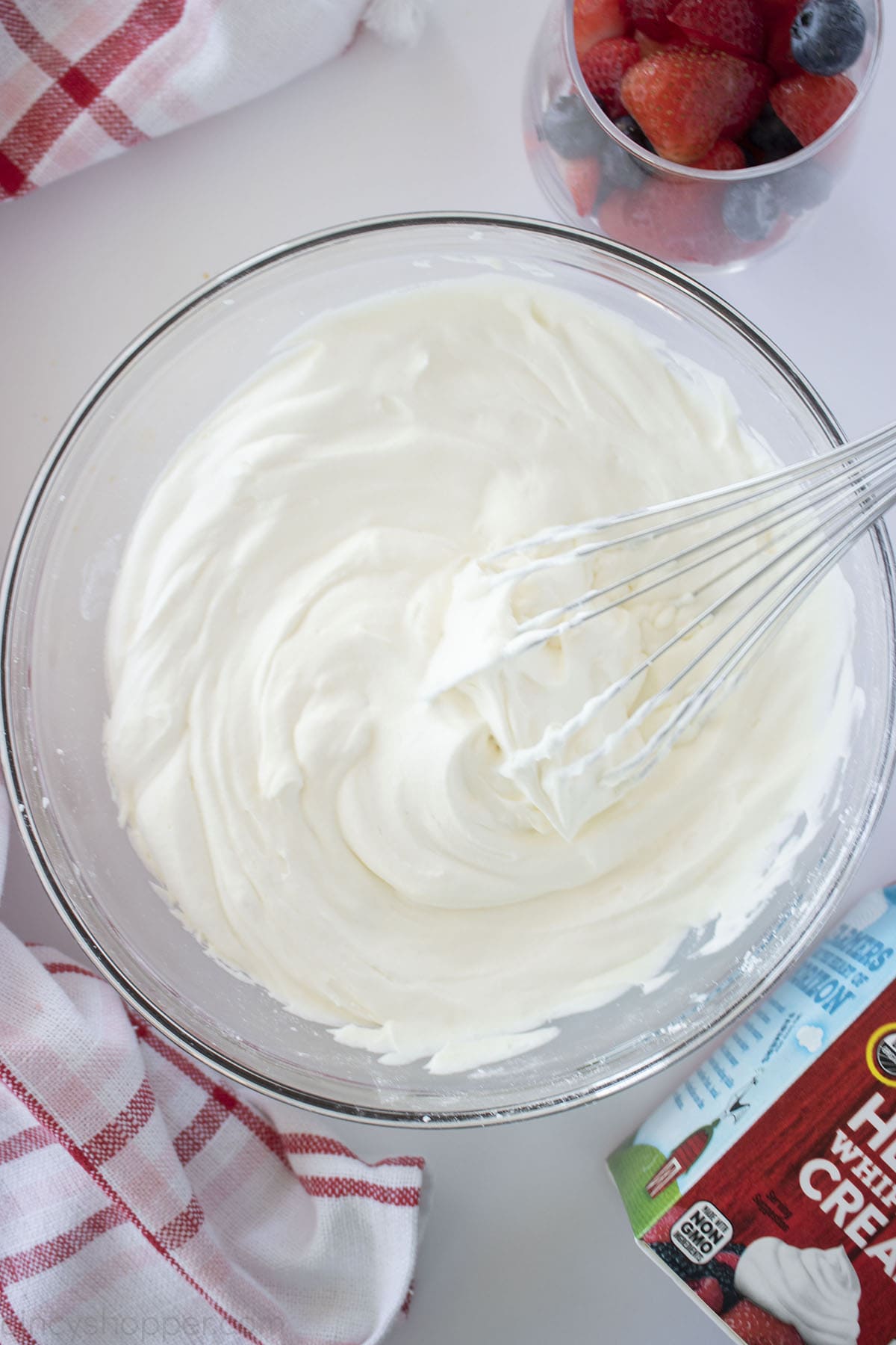 Homemade Whipped Cream in a clear bowl with fruit on the side.