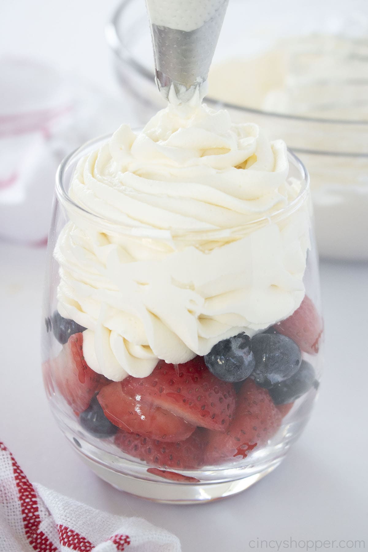 Easy Whipped Cream in a piping bag with a cup of fruit.