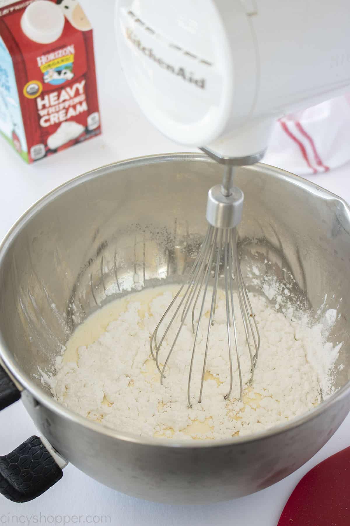 Whipped cream from scratch ingredients in a stainless mixing bowl with hand held mixer.