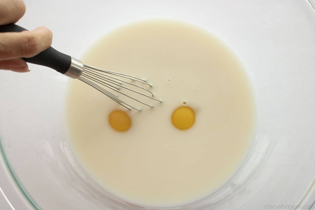 Egg added to milk mixture in a clear mixing bowl.