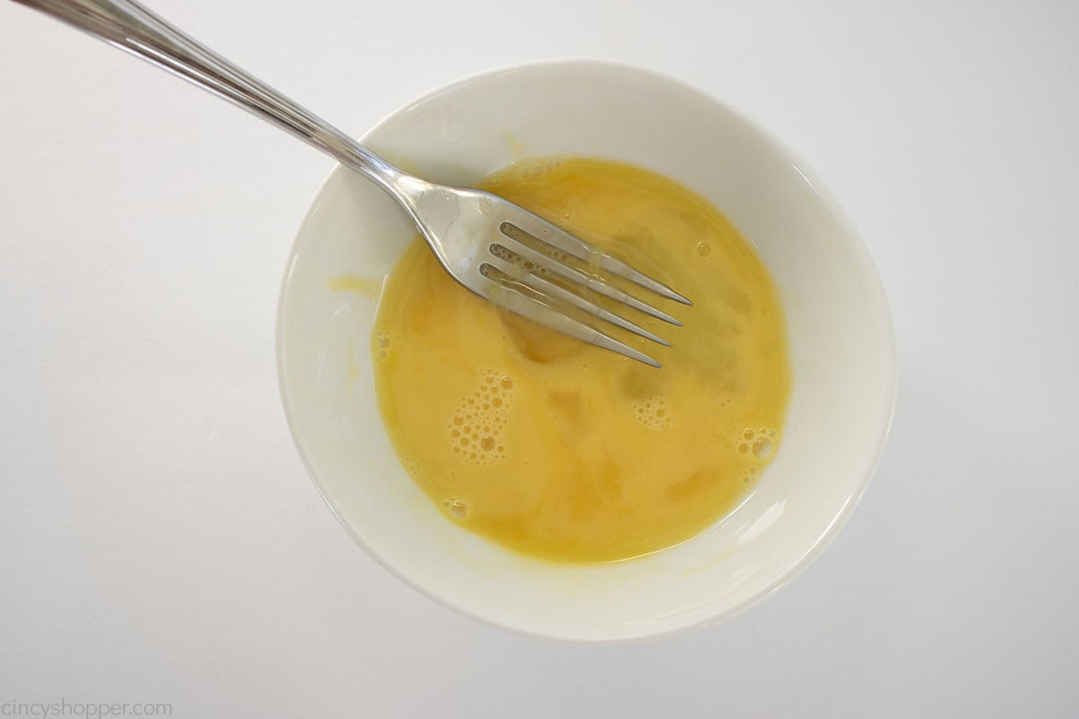 Egg beaten in white bowl with a fork.