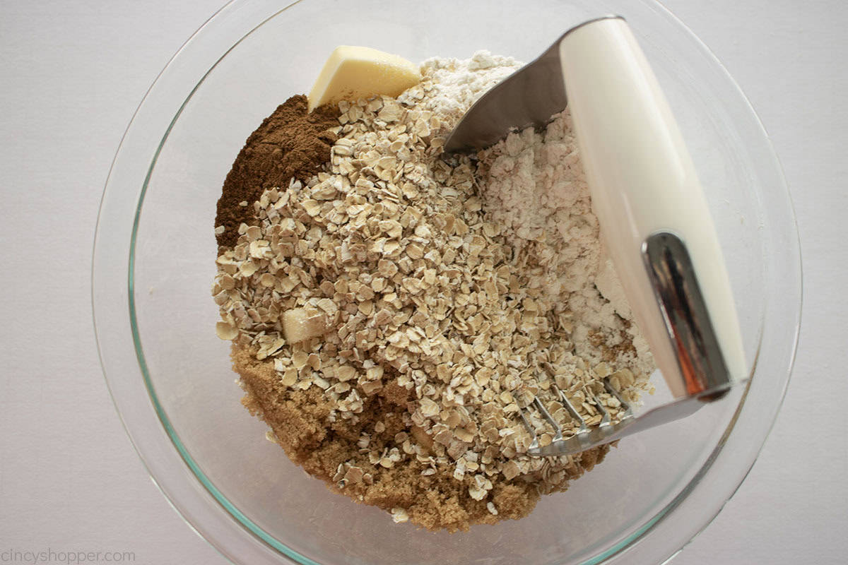 Topping ingredients in a clear mixing bowl with a pastry cutter.