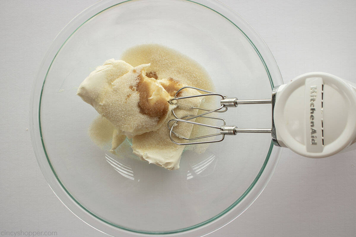 Cream cheese, sugar and vanilla in a clear mixing bowl with hand mixer.