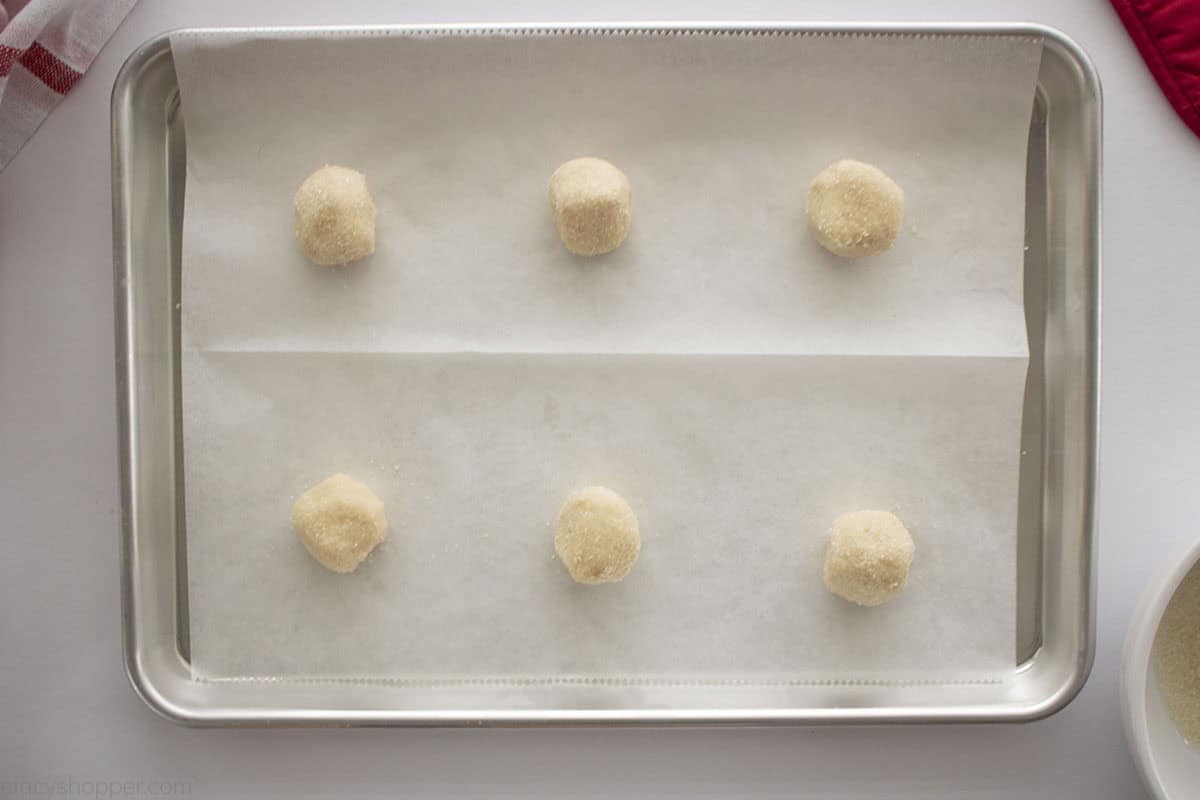 Sugar cookie balls rolled in sugar on a baking sheet.