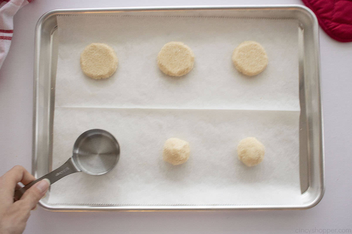 Flattening sugar cookie dough balls with a measuring cup.