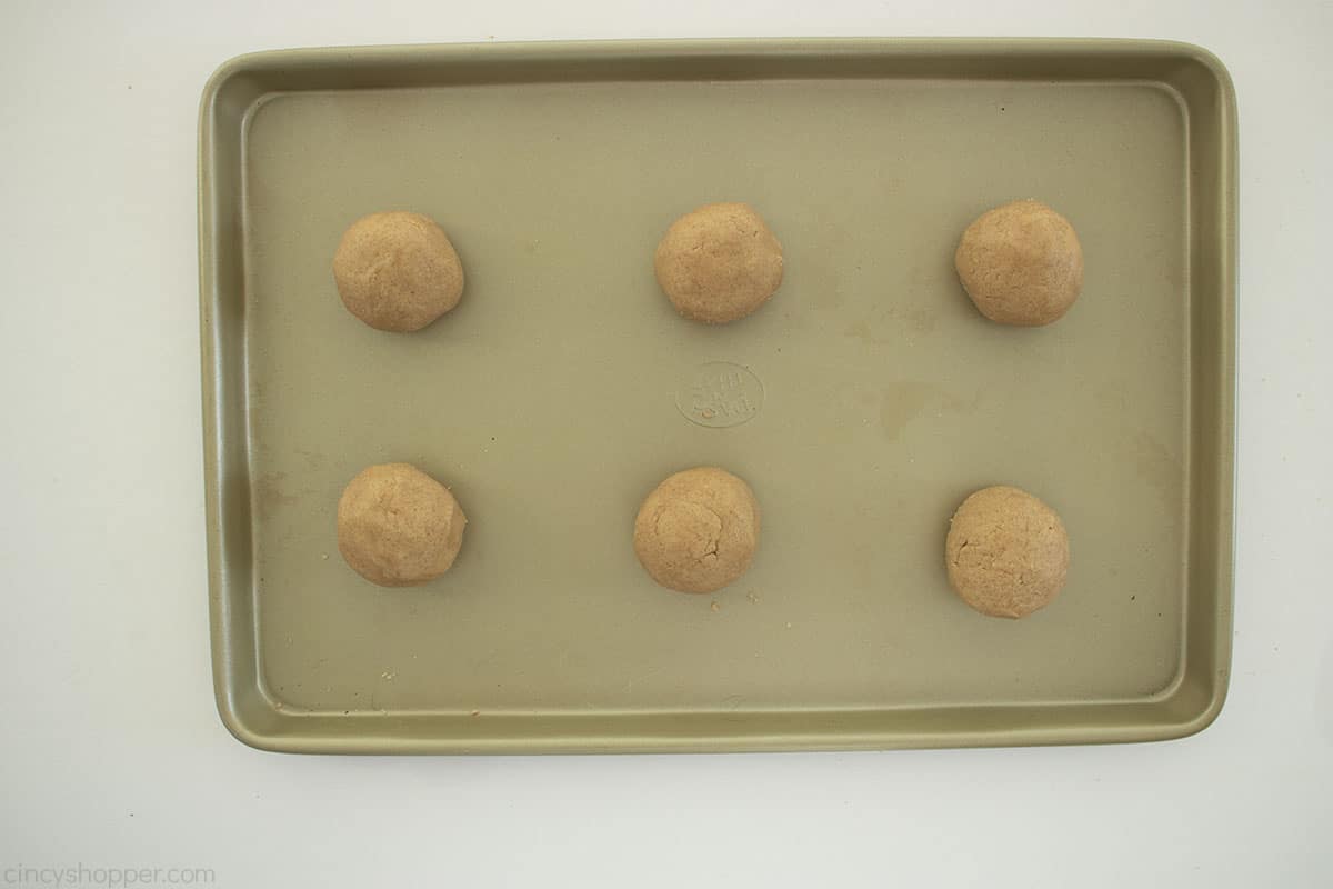 Six round apple pie cookie dough balls on a cookie sheet.