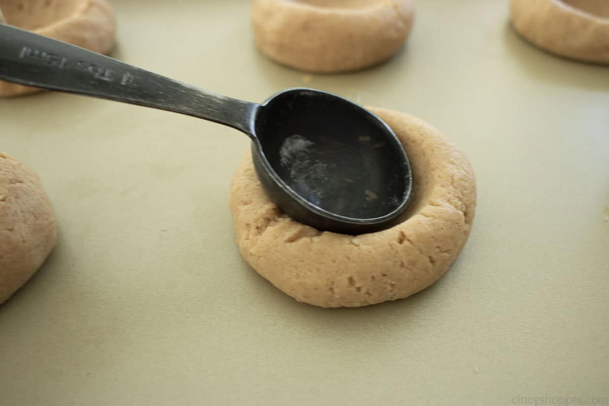 Measuring spoon pressing into cookie to make a "thumbprint"