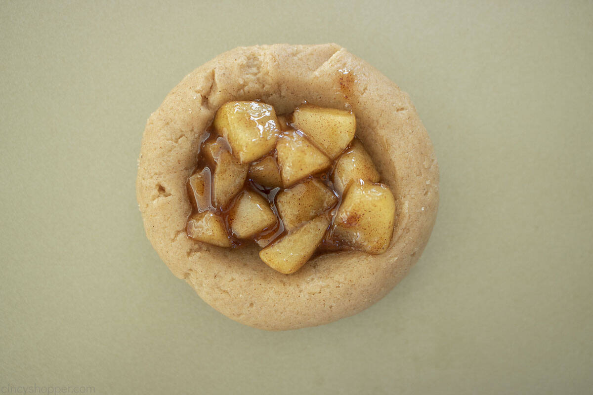 Apple pie filling in tumbprint of cookie dough.